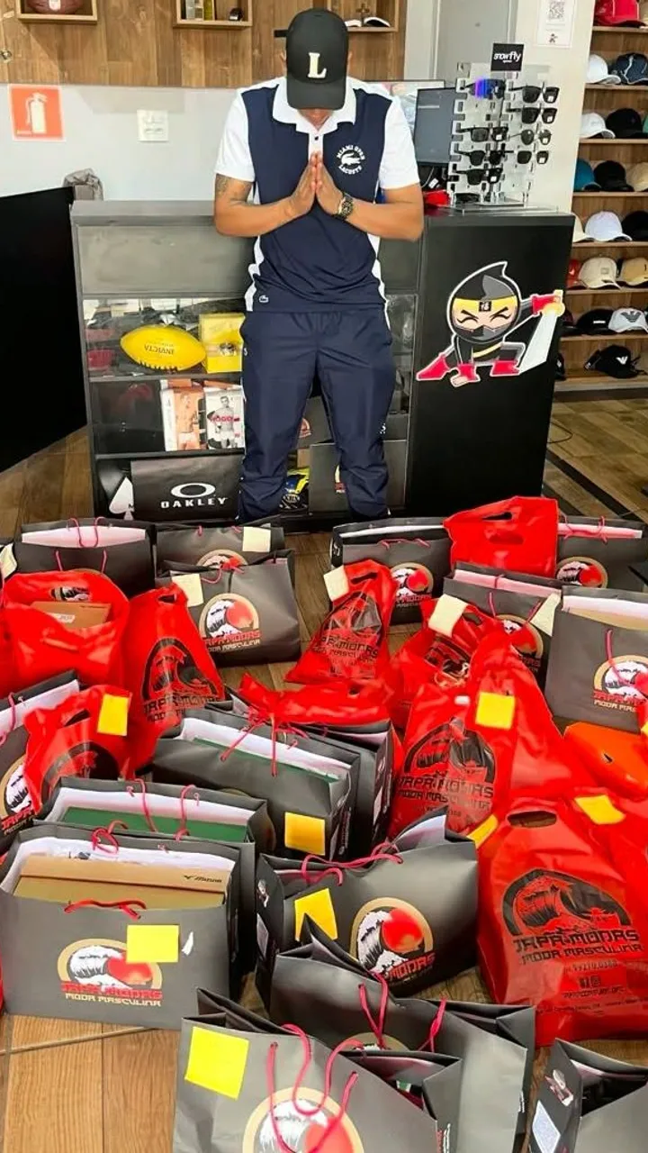 O Japa agradecendo na frente de dezenas de sacolas vermelhas e pretas da loja, com os pedidos da live